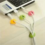 Multi-colored silicone adhesive cable management clips on a wooden desk.