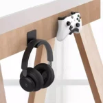 Black adhesive headphone hook holding over-ear headphones under desk