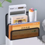 Black metal mesh desk organizer with three compartments holding office supplies.