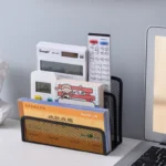 Black metal mesh desk organizer with three compartments holding office supplies.